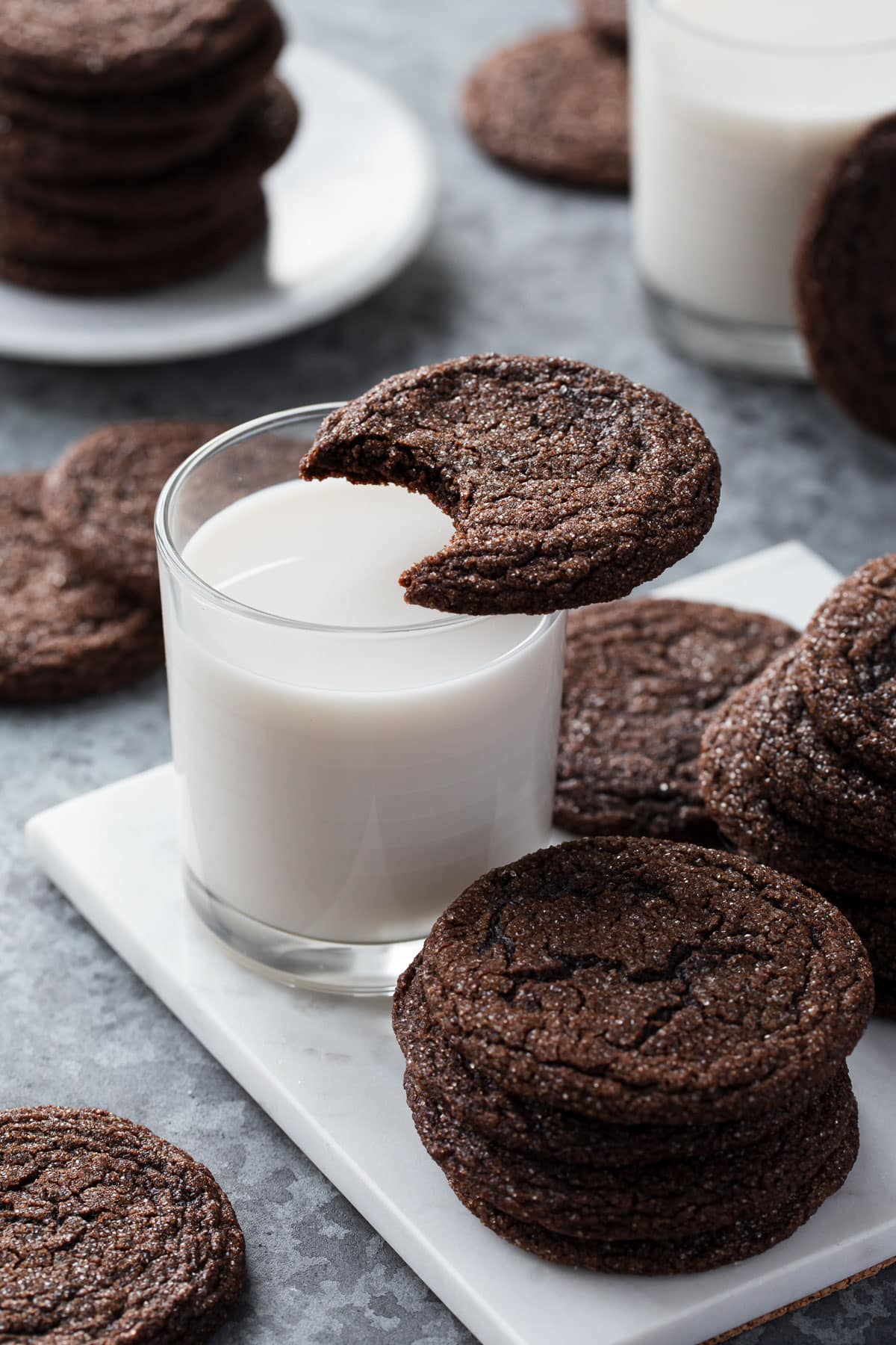 Chewy Chocolate Molasses Cookie with a bite taken out of it resting on top of a glass of milk, more cookies arranged around it.