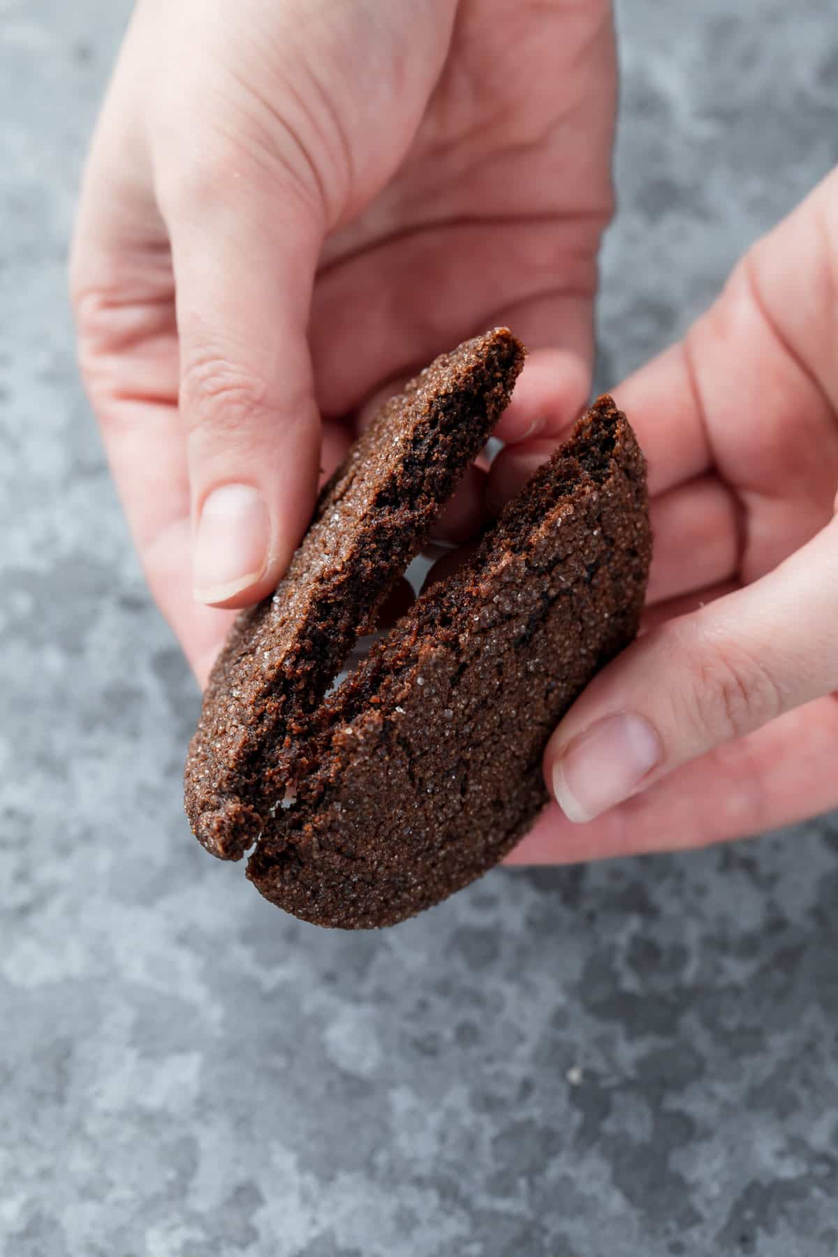 Hands breaking a Chewy Chocolate Molasses Cookie in half to show the chewy, fudgy texture.