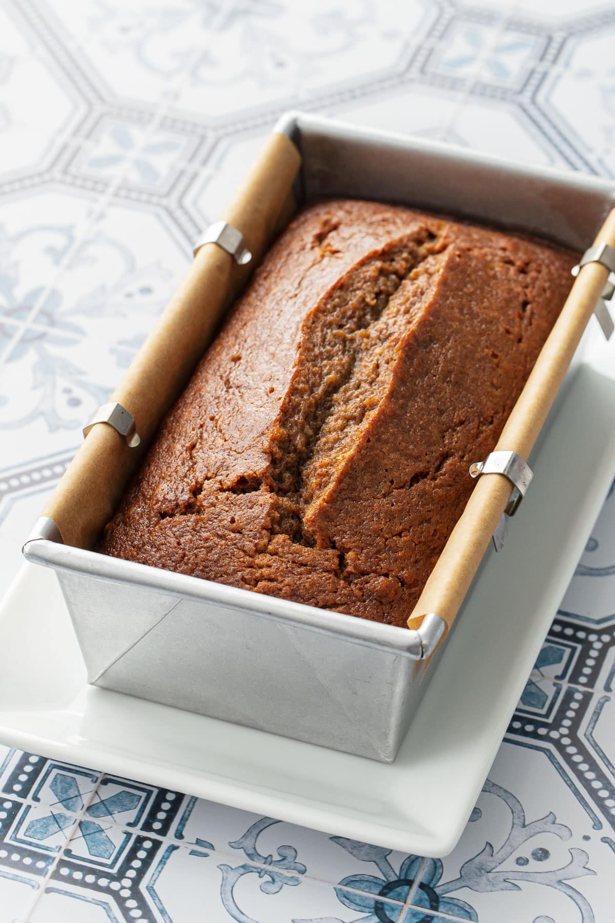 Loaf of freshly baked Spiced Persimmon Bread with a perfectly peaked top, in an aluminum loaf pan lined with parchment paper.