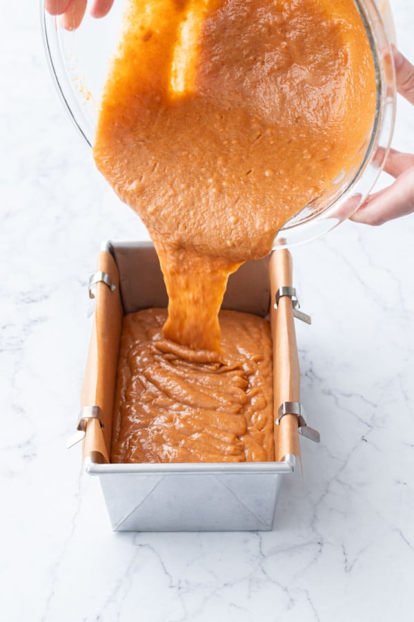 Pouring persimmon bread batter into prepared parchment-lined loaf pan.