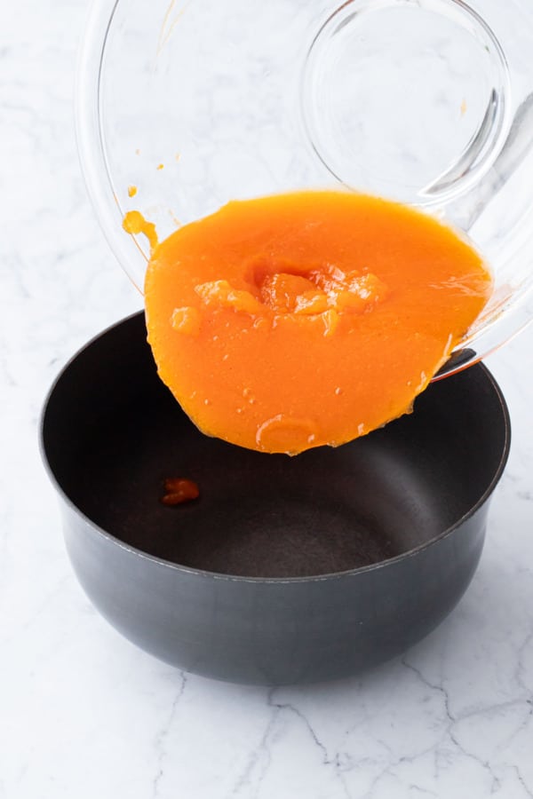 Pouring gelled persimmon into a saucepan.