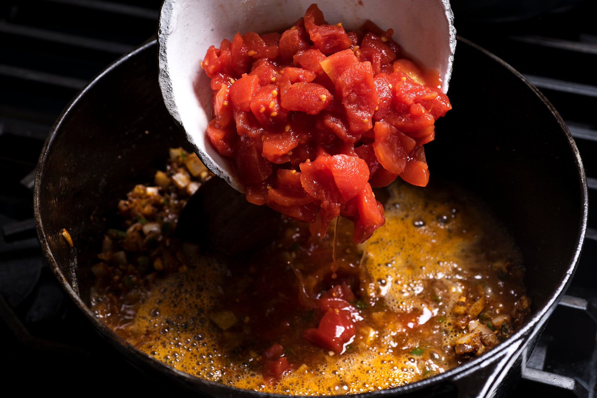 Diced tomatoes are poured into a cast-iron skillet.