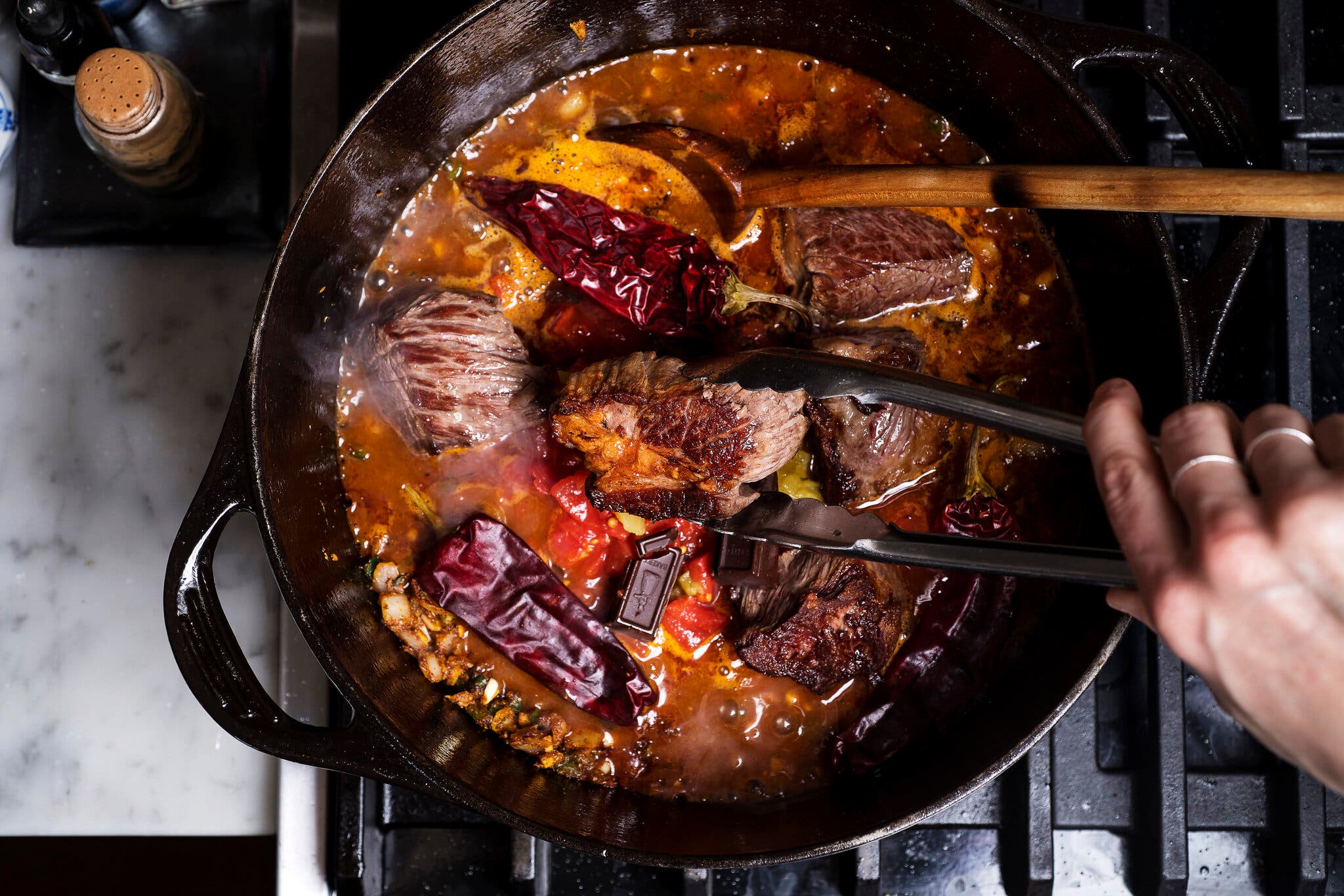 A pair of tongues add the meat back into the skillet, photographed from overhead.