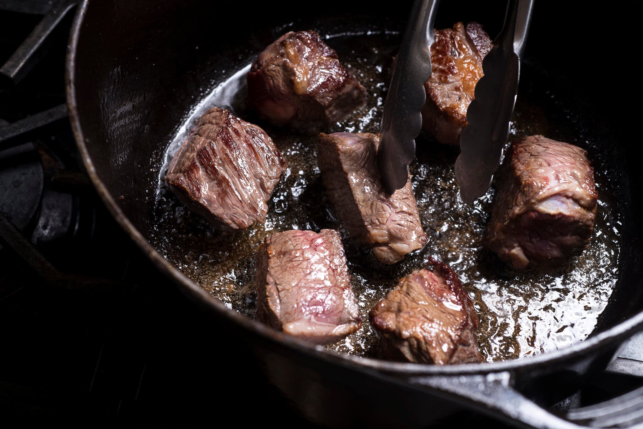 Chunks of beef are seared in a cast-iron skillet.