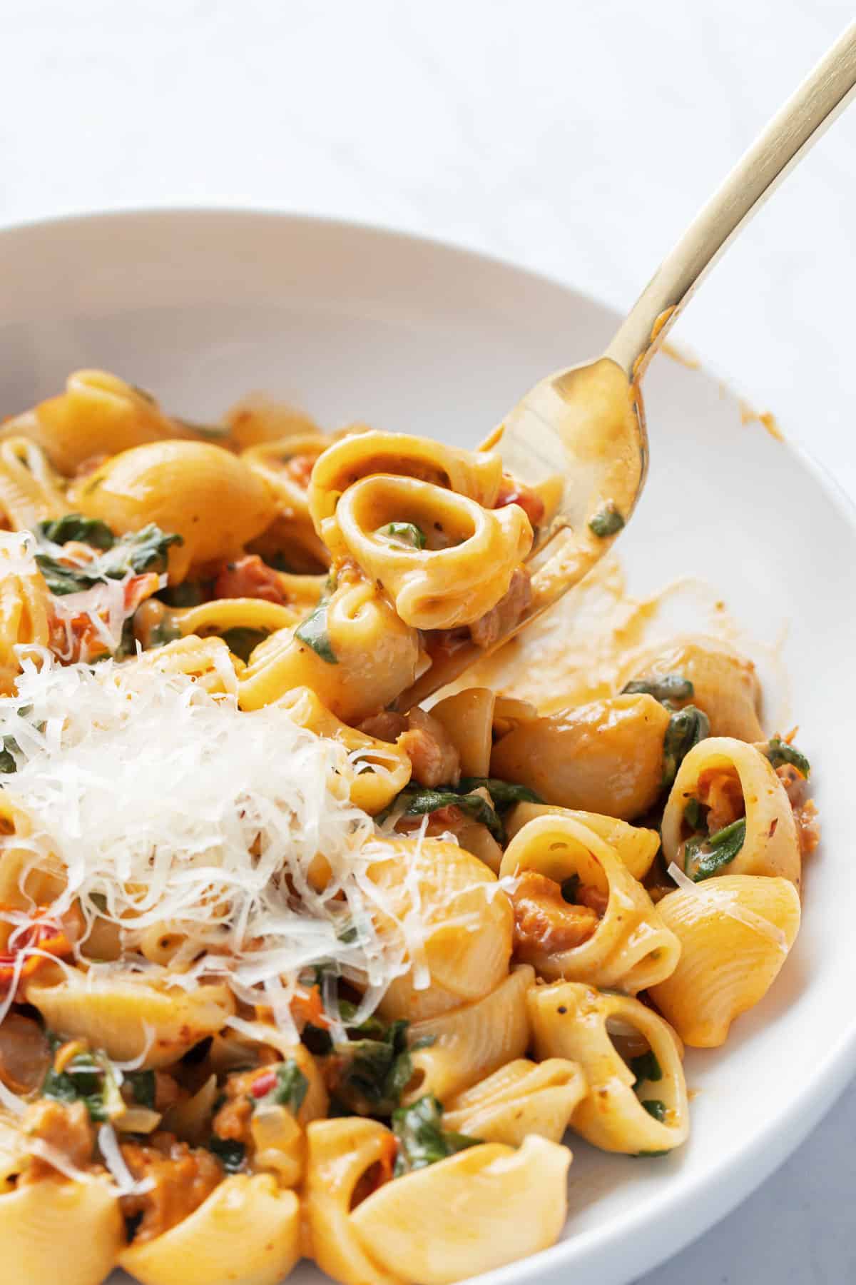 Creamy Sundried Tomato and Italian Sausage Pasta in a white bowl with a gold fork lifting a bite out of the bowl.