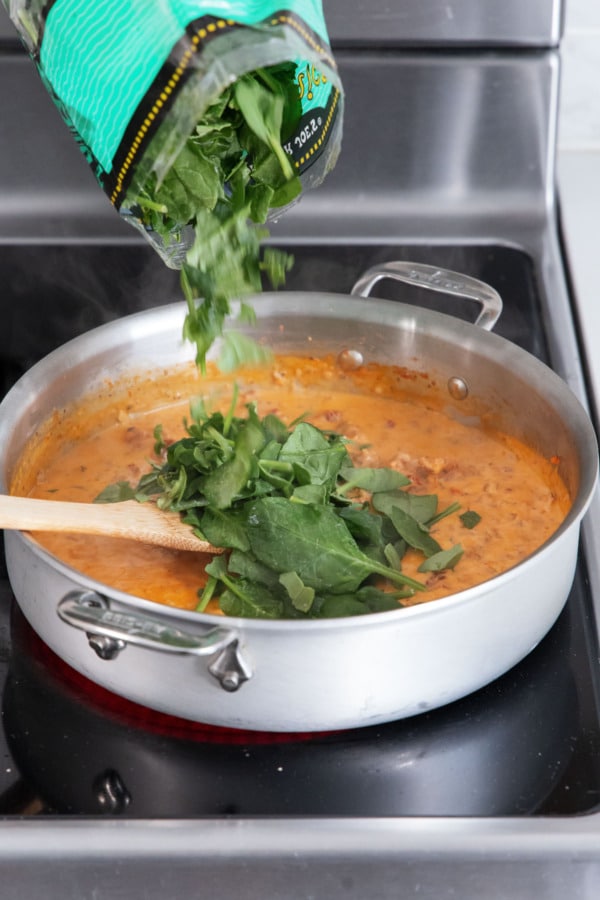 Adding frozen chopped spinach to saucepan with other sauce ingredients.