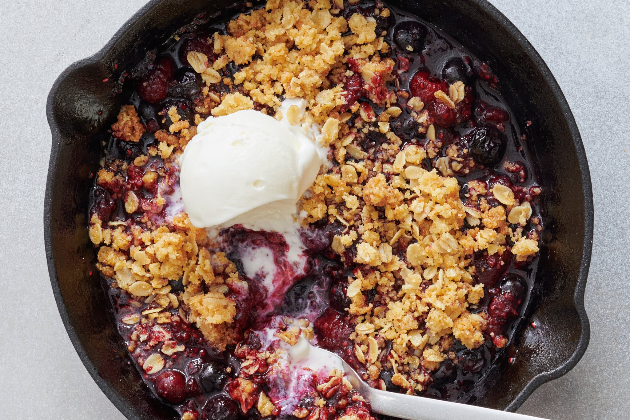 An overhead image of an ice cream topped jammy berry crisp in a cast-iron skillet.