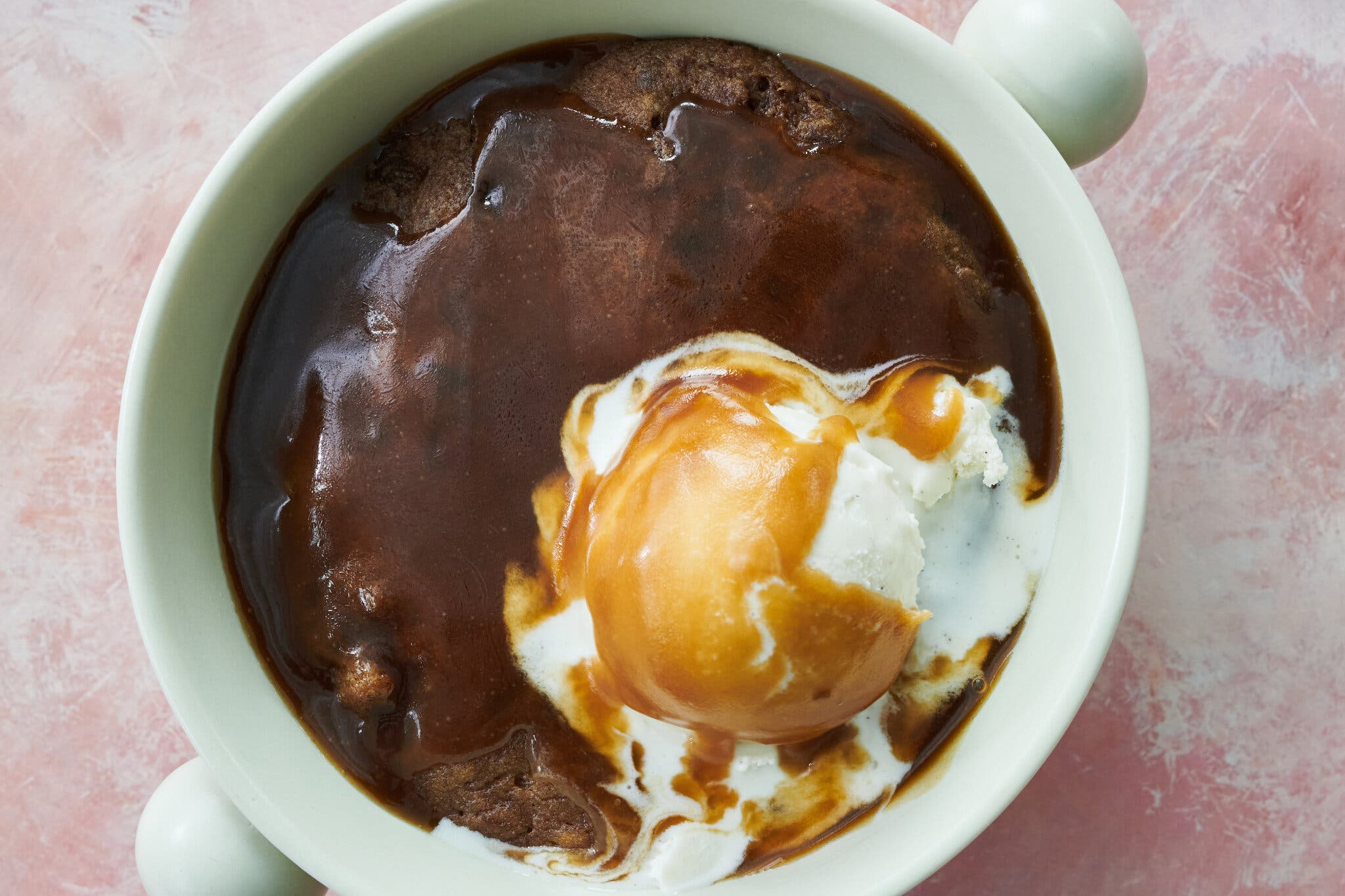 An overhead image of a saucy sticky toffee pudding topped with a melting scoop of ice cream.