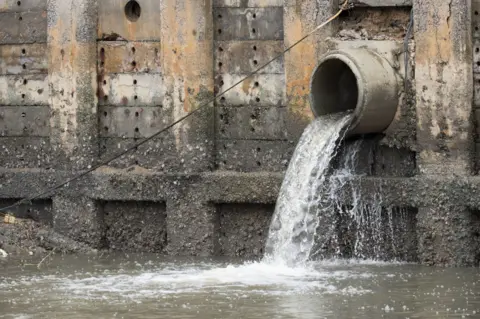 Getty Images Storm overflow pipe spills water into brown-coloured river