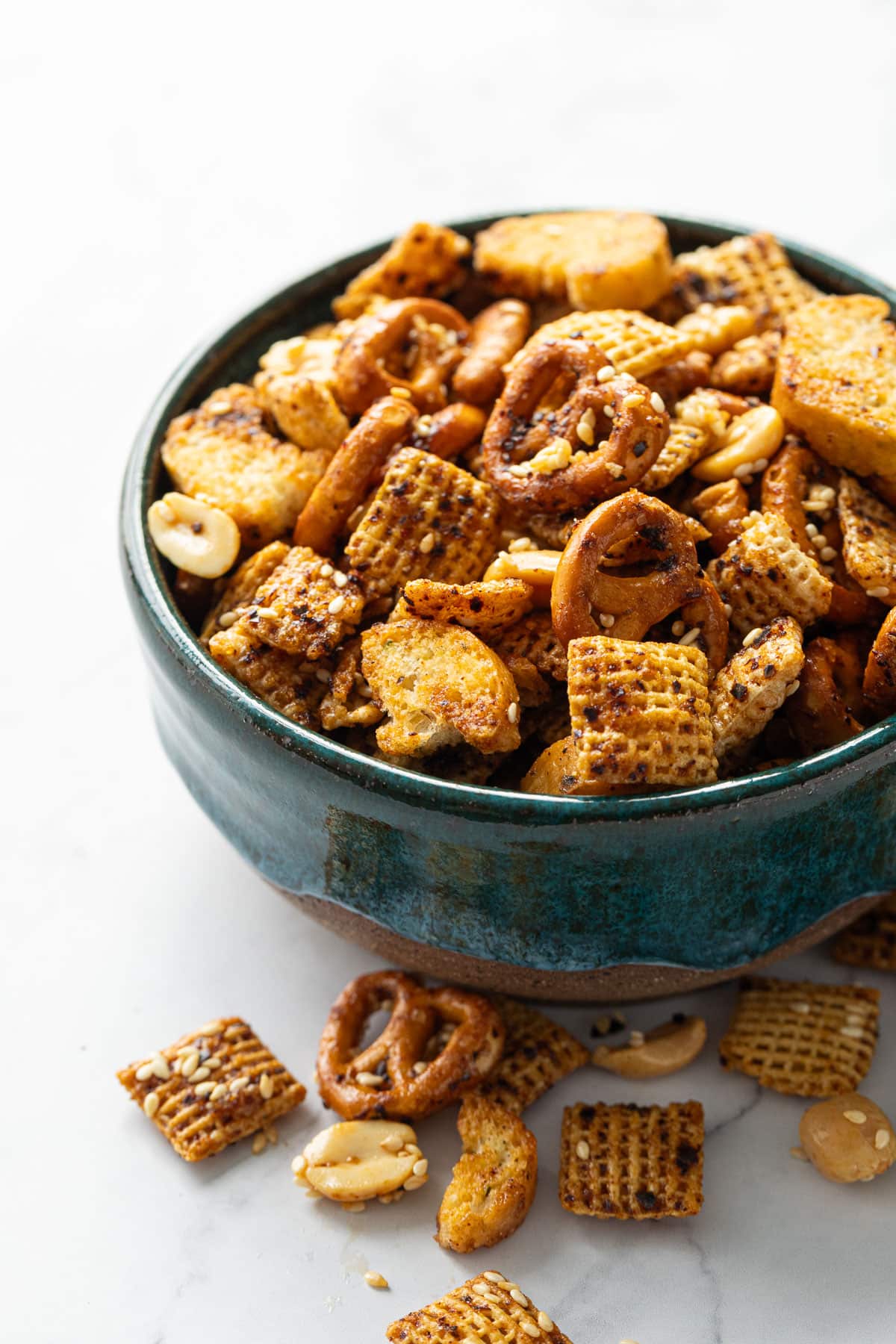 Teal ceramic bowl overflowing with homemade sesame snack mix on marble background.