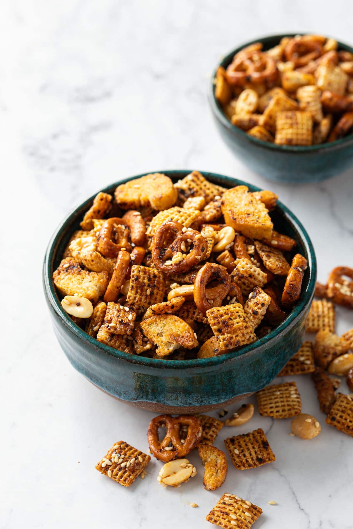 Two teal ceramic bowls overflowing with homemade snack mix on. marble background.