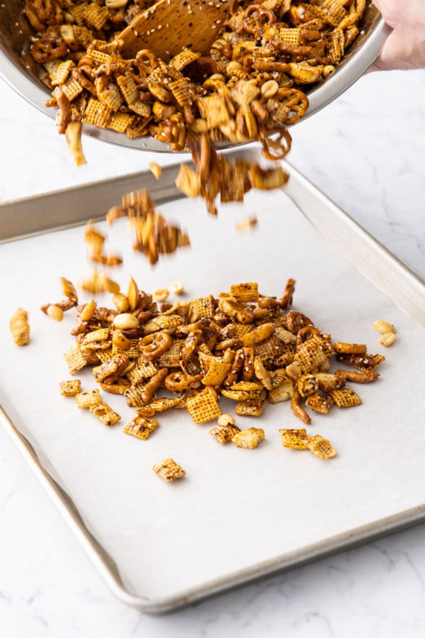 Pouring snack mix onto a parchment lined baking sheet.