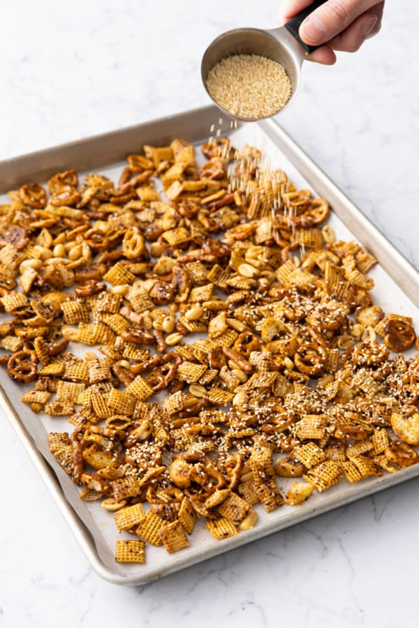 Sprinkling snack mix with sesame seeds just before baking.