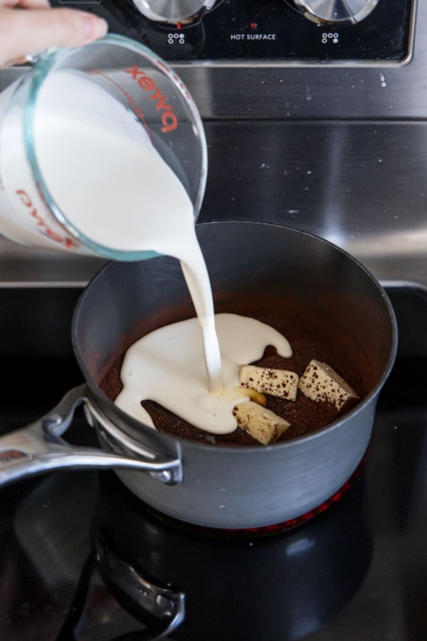 Pouring heavy cream into saucepan with other frosting ingredients.