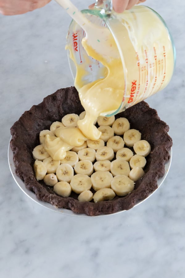 Pouring the first layer of vanilla custard on top of the banana slices in the pie crust.