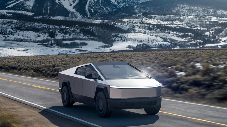 A Tesla Cybertruck seen in front three-quarter view while driving in a snowy landscape