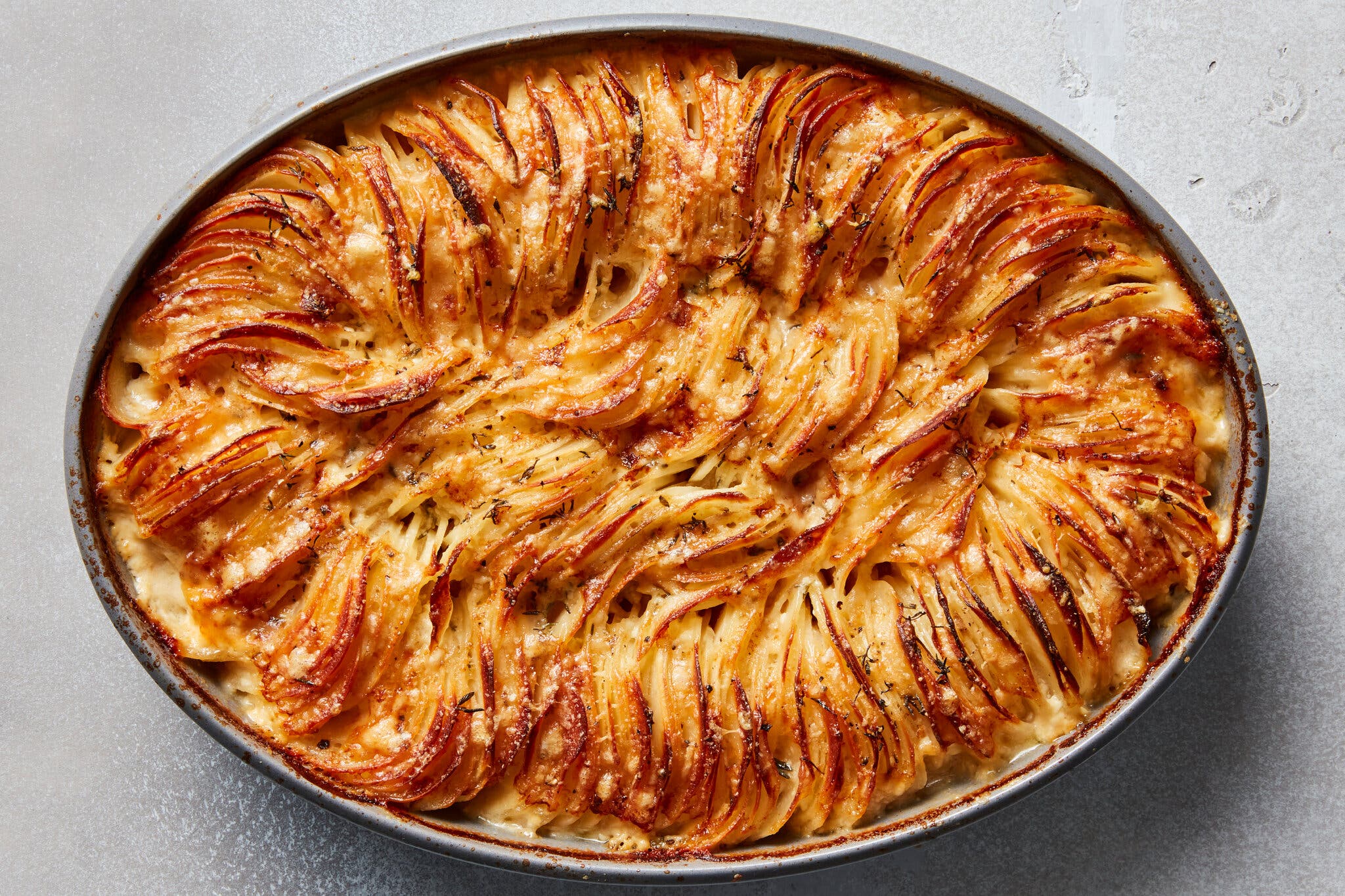 An oval baking dish filled with thinly sliced, golden-brown scalloped potatoes in layers.