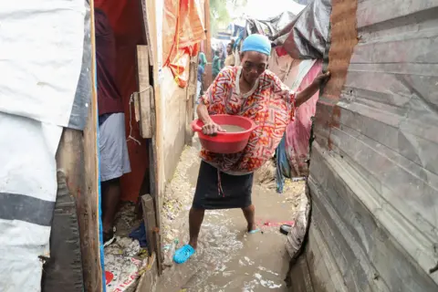 Reuters A woman wading through liquid mud carries a bowl of water out of her flooded home in Port-au-Prince, Haiti on 29 October.