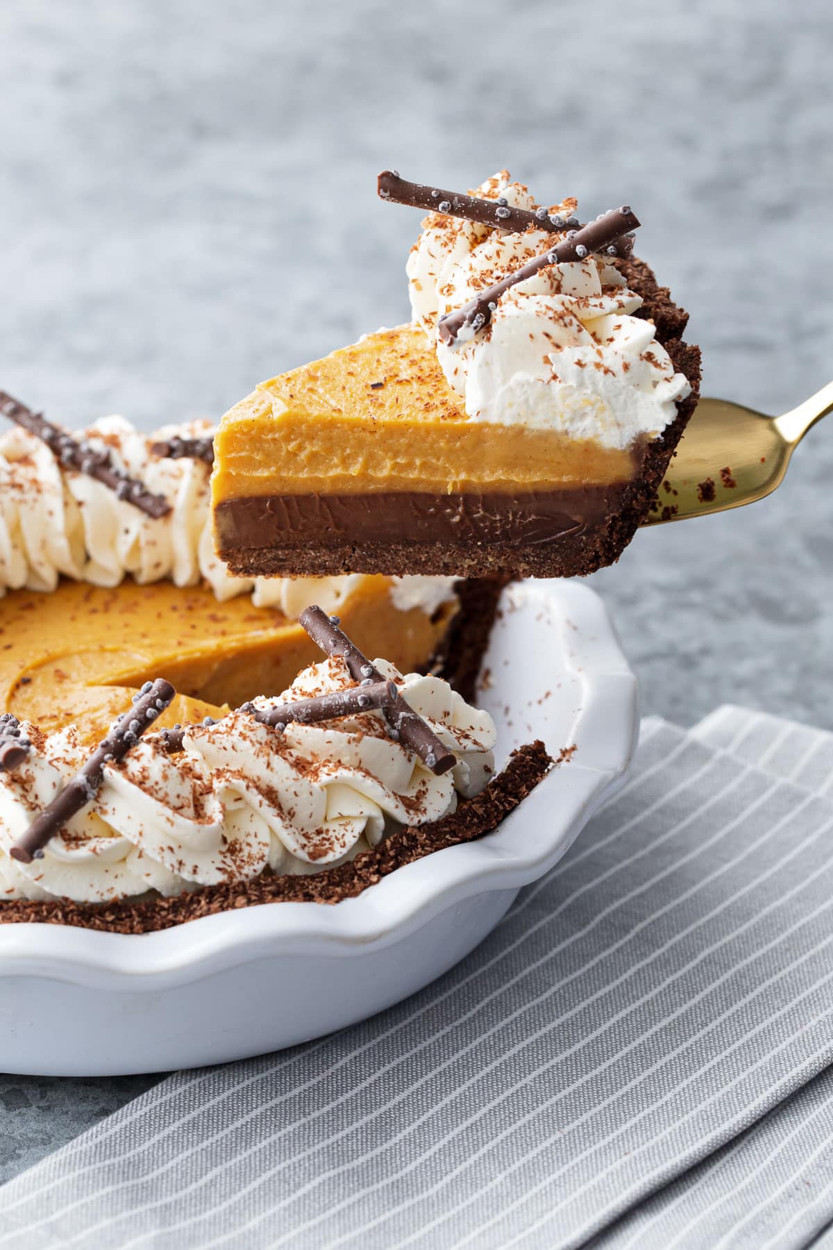 Lifting a slice of Black Bottom Pumpkin Cream Pie out of the pie plate, showing the distinct layers of chocolate ganache and pumpkin cream.