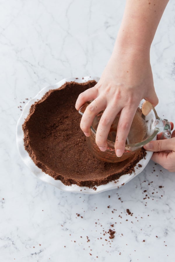 Using a measuring cup to press the crumbs into the pie pan firmly up the sides.