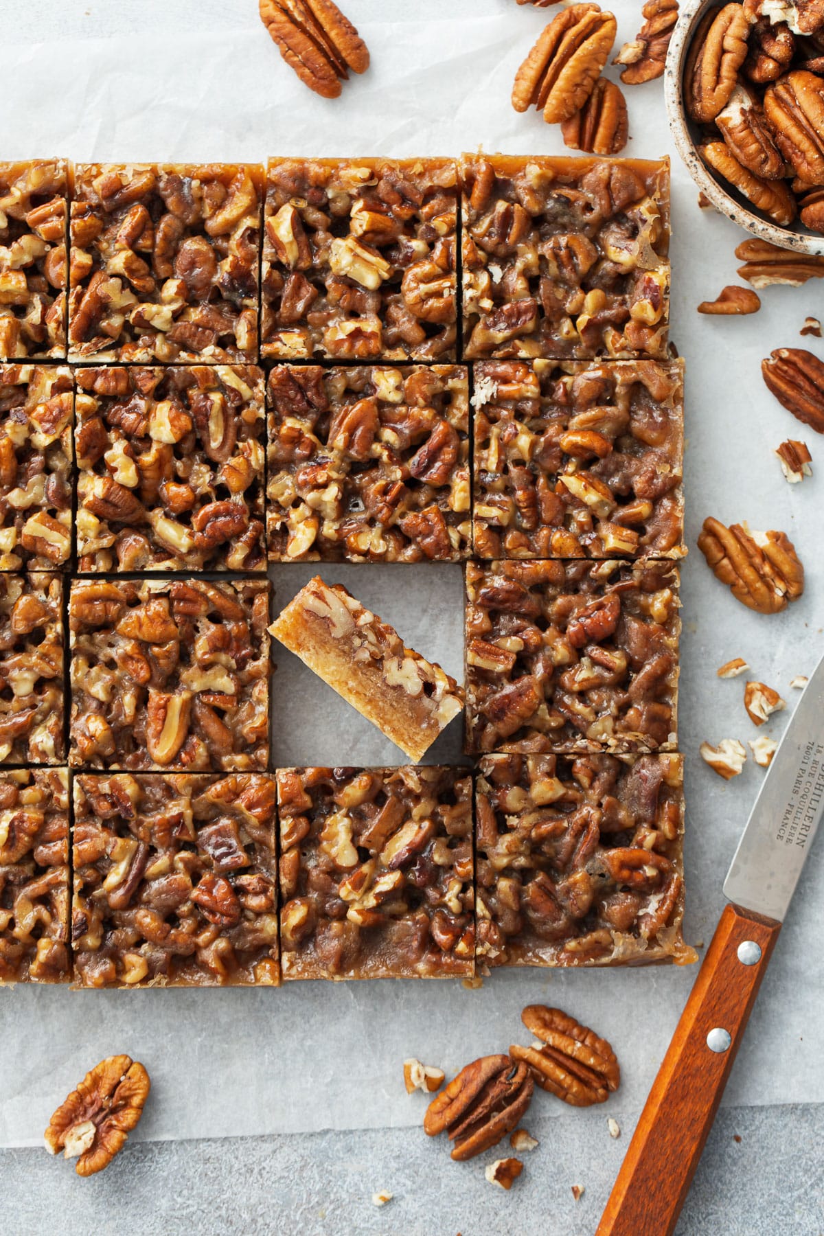 Overhead, square cut Pecan Pie Shortbread Cookie Bars on parchment, one tilted on its side to show the layers.
