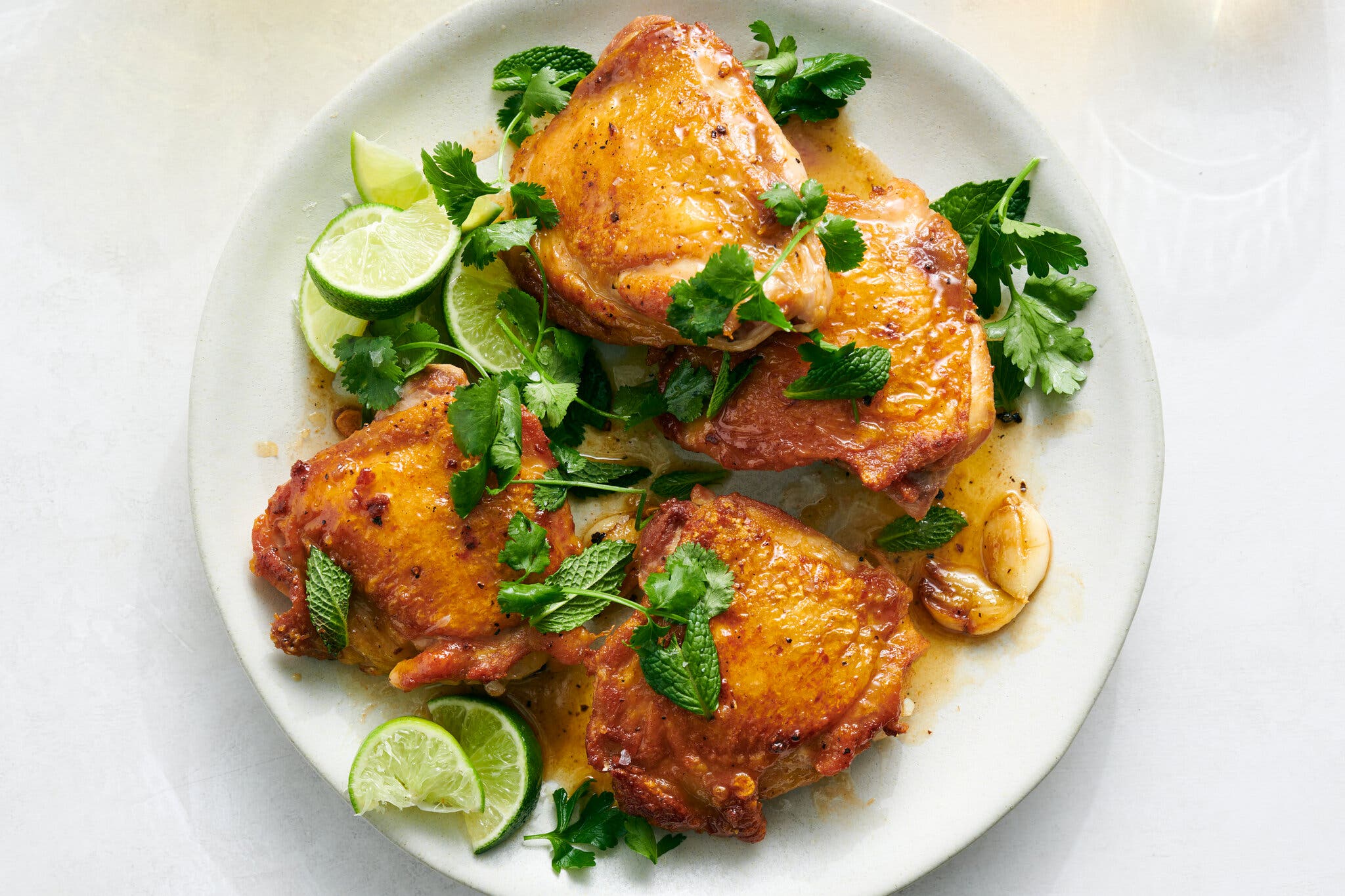 An overhead image of four chicken thighs surrounded by lime wedges and herbs.
