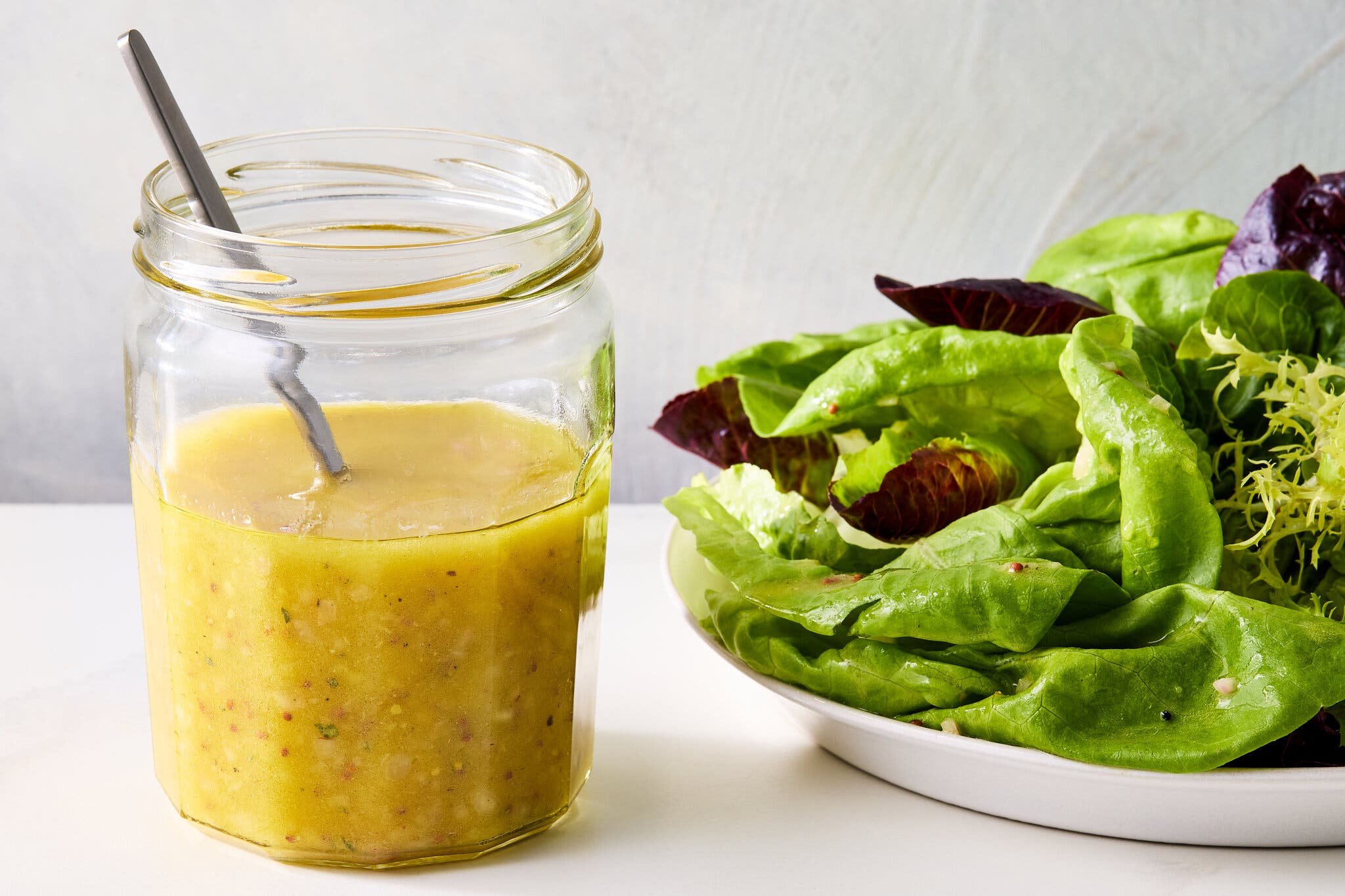A side image of a yellow dressing in a jar next to some greens.