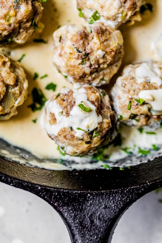 These easy Swedish meatballs are a lighter version of the classic, but they have the same cozy, comforting flavor and creaminess you love! Closeup of creamy Swedish meatballs with gravy in cast iron skillet.