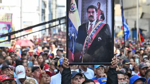 Getty Images A supporter of ousted Venezuela's President Nicolas Maduro carrieshis portrait during a rally outside the National Assembly in Caracas on Monday. Hundreds of people can be seen in the crowd. In the portrait of Maduro he is wearing a black suit, red tie and a sash bearing the colours of the Venezuelan flag. 